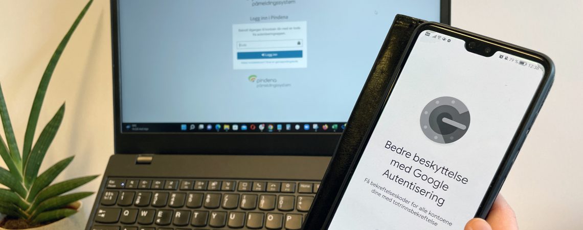 Mobil med forsidebilde av Google Authenticator og laptop med innlogging til Pindena i bakgrunnen