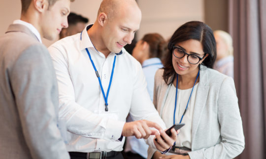 Tre personer på konferanse som ser på en telefon sammen