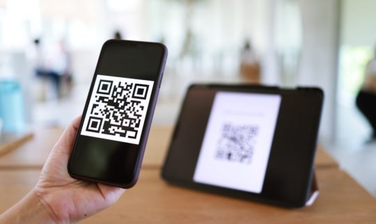 En mobil med en QR-kode holdes opp foran en skjerm med QR-kode for registrering.