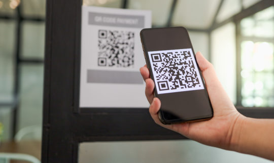 En person bruker en mobiltelefon for å scanne en QR-kode ved innsjekk