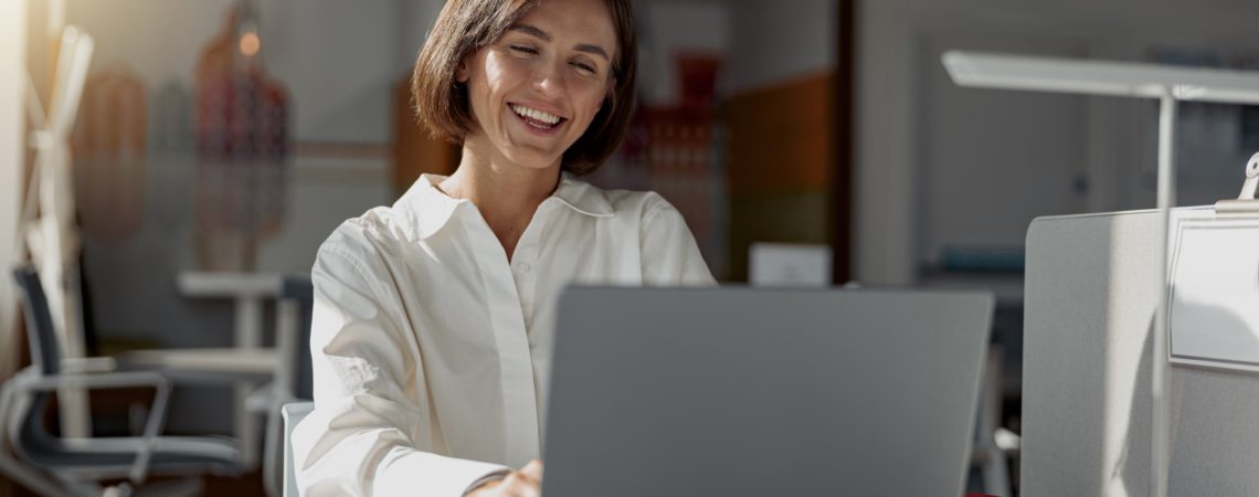 Smilende dame som jobber med fakturering på laptop i et rolig kontormiljø.