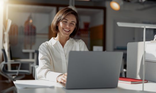 Smilende dame som jobber med fakturering på laptop i et rolig kontormiljø.