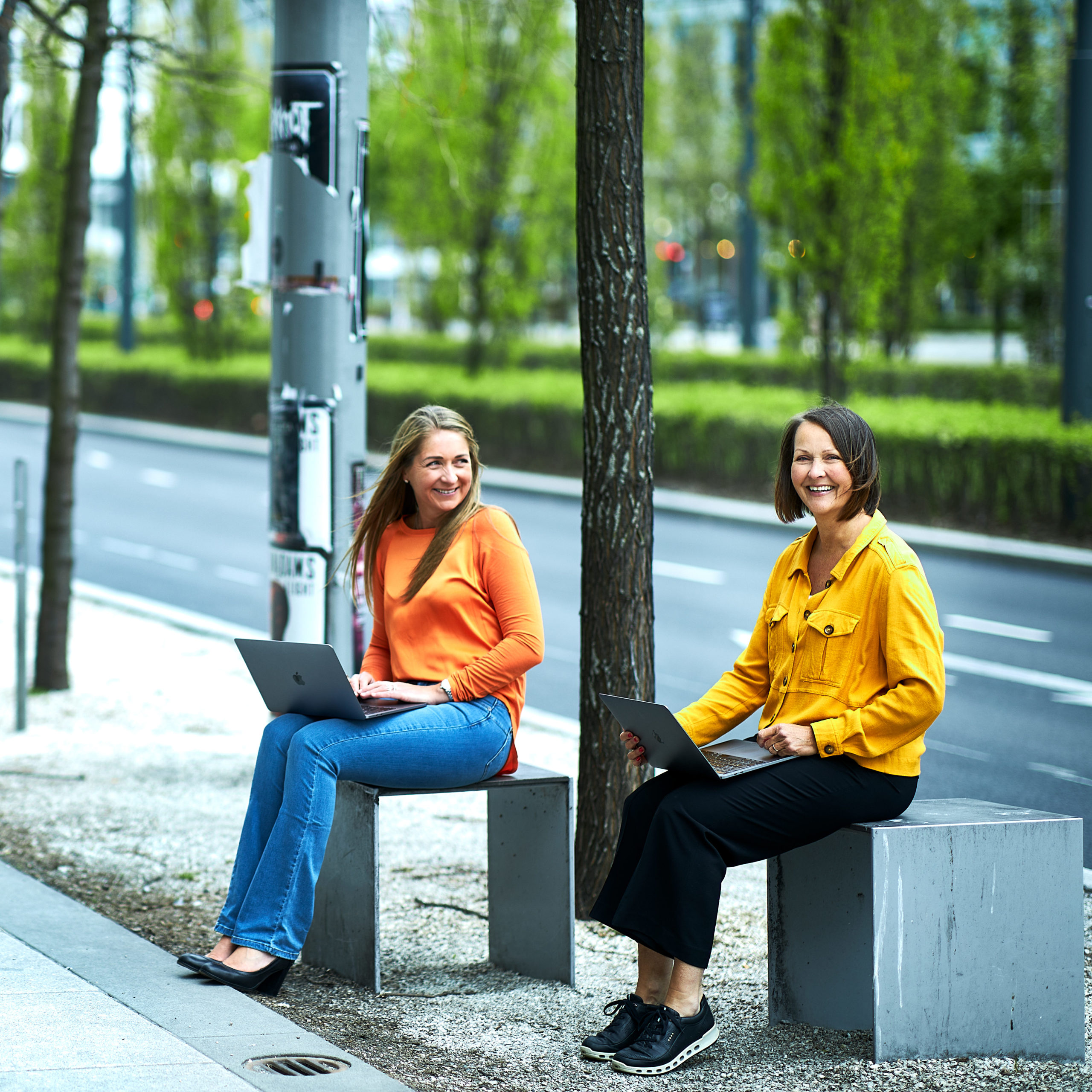 Benedicte og Sølvi Anne i CRED sitter på hver sin benk langs et fortau, med hver sin laptop i fanget